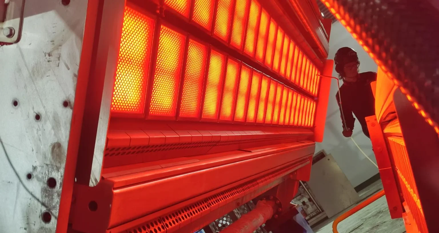 Worker inspecting an active industrial infrared drying system glowing red.