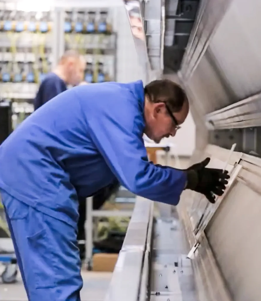 Person in blue workwear inspecting industrial equipment.